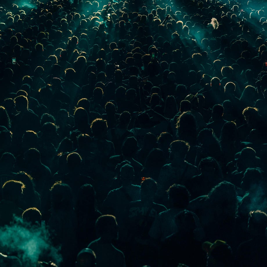 A dense crowd enjoys a lively concert at night with dramatic lighting creating shadows and an energetic atmosphere.